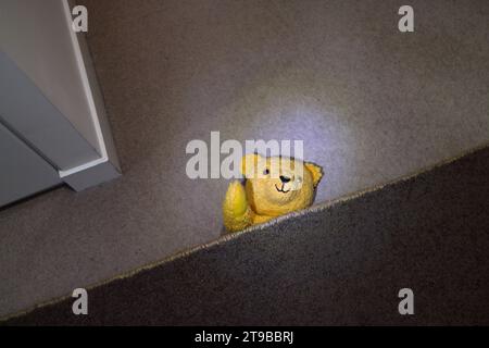 Yellow teddy bear toy doll hiding and waving from under a rug Stock Photo