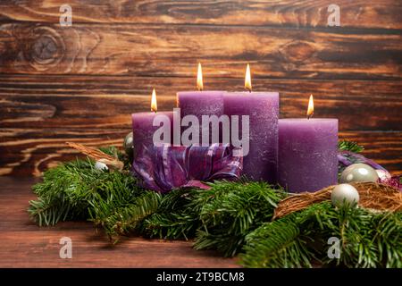 Augsburg, Bavaria, Germany - November 24, 2023: Christmas wreath with four burning purple candles for Advent *** Weihnachtskranz mit vier brennenden lila Kerzen zur Adventszeit Stock Photo