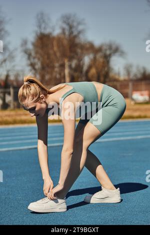 beautiful sportswoman in activewear tying laces on white sneakers before running in jogging track Stock Photo