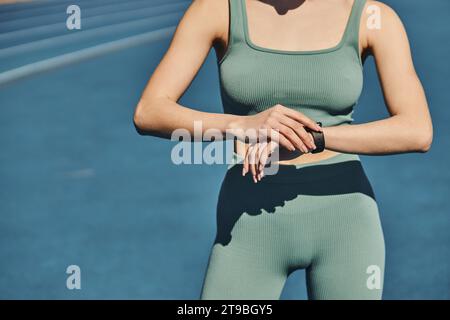 cropped sportswoman in activewear standing and checking her fitness tracker in jogging track Stock Photo