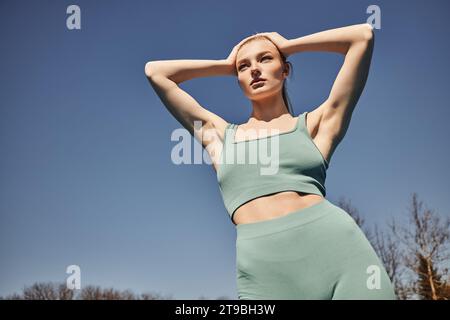 Low angle side view of young fit female in sports bra and leggings running  fast along sandy seashore during fitness workout in summer day stock photo