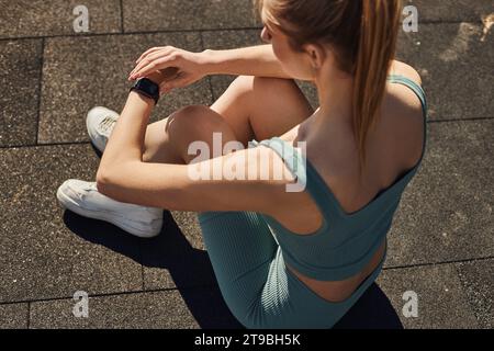 top view of young sportswoman in activewear sitting and checking fitness tracker after workout Stock Photo