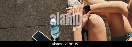 banner of sportswoman in activewear checking fitness tracker next to smartphone and water bottle Stock Photo