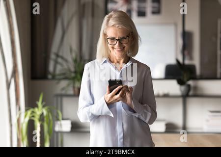 Cheerful blonde senior businesswoman using Internet application Stock Photo