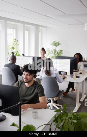 Man wearing headset using desktop PC in office Stock Photo