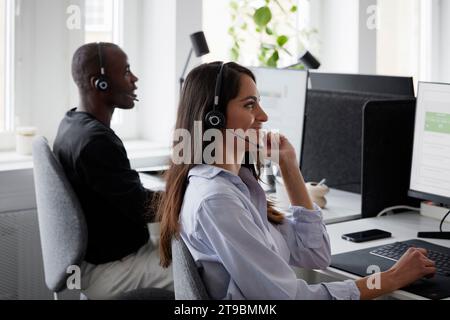 Woman wearing headset using desktop PC in office Stock Photo