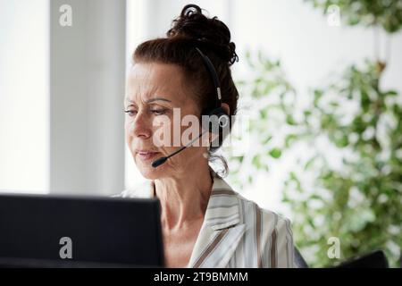 Woman wearing headset using desktop PC in office Stock Photo