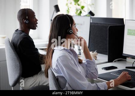 Woman wearing headset using desktop PC in office Stock Photo