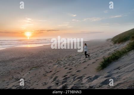 Woman walking on empty beach at sunset Stock Photo