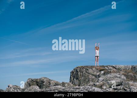 Girl standing on rock formation against blue sky on sunny day Stock Photo