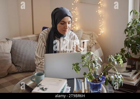 Young businesswoman using smart phone by laptop while working in living room Stock Photo