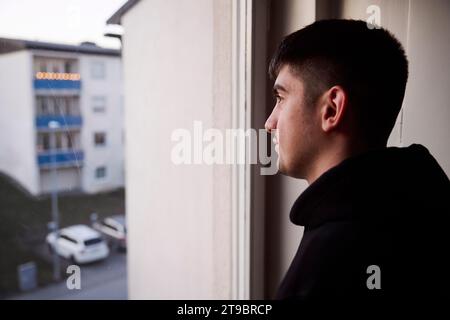 Thoughtful young man looking through window Stock Photo
