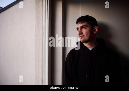 Thoughtful young man looking through window Stock Photo