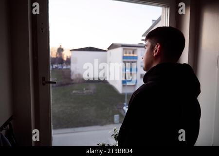 Thoughtful young man looking through window Stock Photo