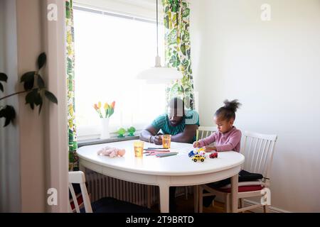 Man and girl sitting at dining table while drawing on papers Stock Photo