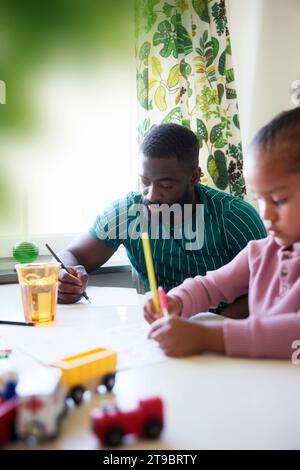 Father and daughter drawing while sitting at dining table Stock Photo