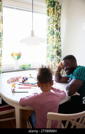 Smiling man leaning on elbow while sitting by daughter Stock Photo