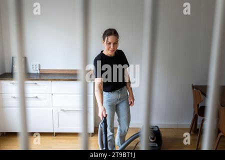 Smiling young woman using vacuum cleaner at home Stock Photo