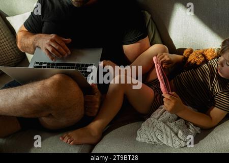 High angle view of male freelancer working on laptop with his son using digital tablet in living room Stock Photo