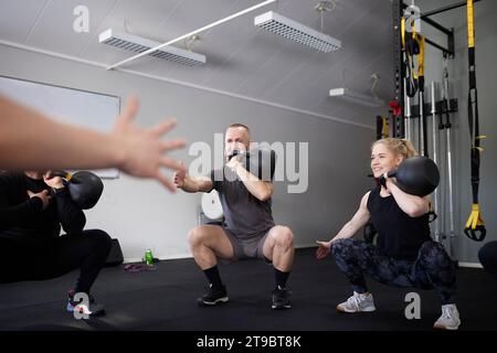Men and woman exercising with kettlebells while squatting in gym Stock Photo