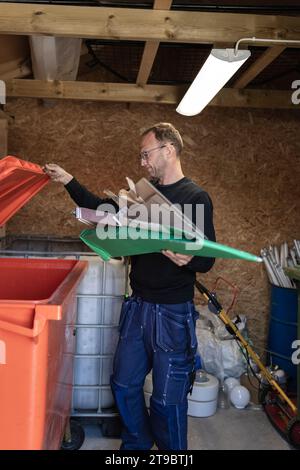 Male blue-collar worker throwing cardboard waste in garbage bin at recycling center Stock Photo