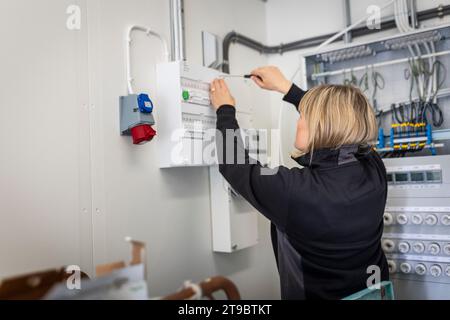 Blond female technician installing fuse box while working in control room of industry Stock Photo