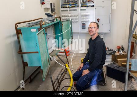 Smiling male electrician kneeling by electric panel in industry Stock Photo