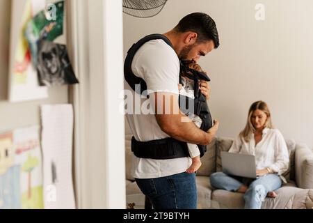 Side view of man kissing son while woman using laptop at home Stock Photo