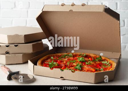 Large Pizza in open carton box and cutter on kitchen table closeup view Stock Photo