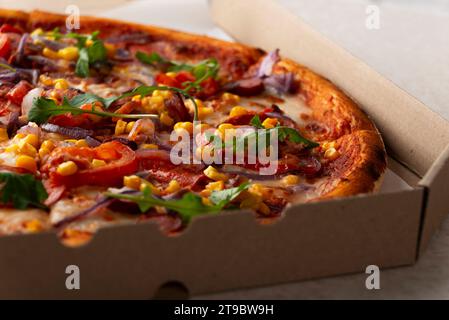 Large Pizza with sausages peppers and sweetcorn in open carton box on kitchen table extreme closeup view Stock Photo