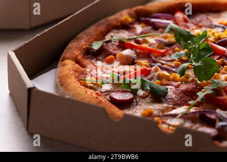 Large Pizza with sausages peppers and sweetcorn in open carton box on kitchen table extreme closeup view Stock Photo