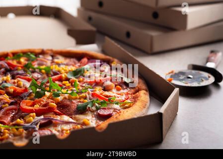 Large Pizza in open carton box and cutter on kitchen table closeup view Stock Photo