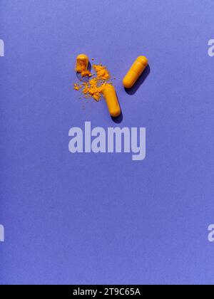 Opened orange pills on violet background Stock Photo