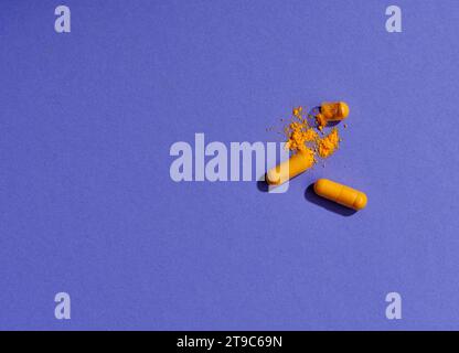 Opened orange pills on violet background Stock Photo