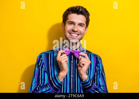 Portrait of pleasant cheerful gentleman dressed stylish shirt touching bow tie smiling isolated on vibrant yellow color background Stock Photo