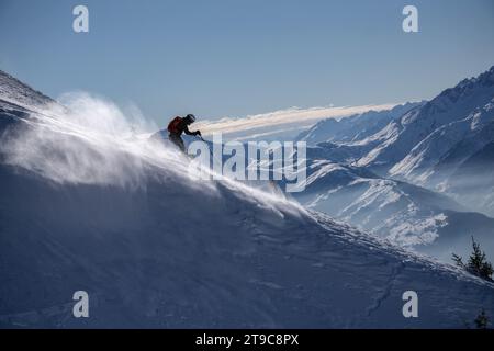 Boy skiing down the mountains, creating a flurry of white snow powder as he descends.Mountains and a blue sky in the background. France, Franch Alps. Stock Photo