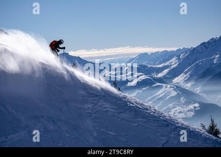 Boy skiing down the mountains, creating a flurry of white snow powder as he descends.Mountains and a blue sky in the background. France, Franch Alps. Stock Photo