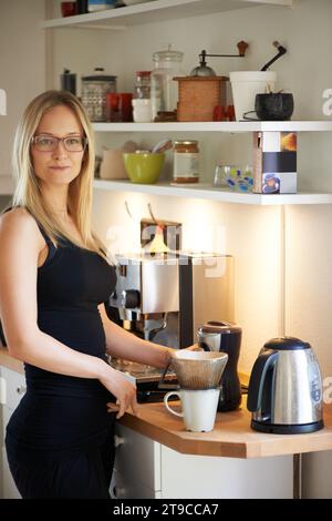 Portrait, woman and cup for making coffee in kitchen with filter for strong, delicious and taste. Person, spectacles or glasses for vision with mug Stock Photo