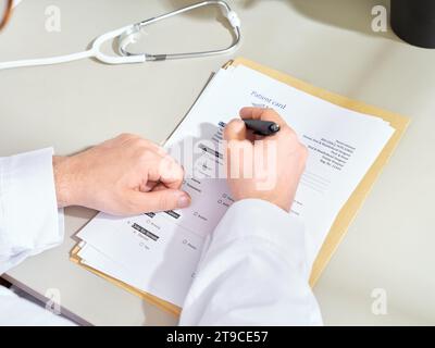 Anonymous male doctor in a white gown filling out medical documentation in a clinic Stock Photo