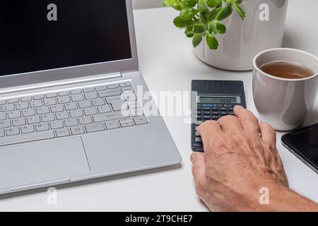 Close-up of senior man using calculator and laptop on white table Stock Photo