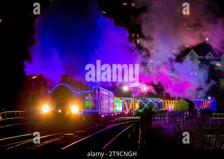 Kingswear, Devon, UK.  24th November 2023.   The Christmas Train of Lights on the Dartmouth Steam Railway which runs between 24th November to 30th December 2023, pulls out of Kingswear station in Devon on its way to Paignton.  The carriages and steam locomotives on the festive service are lit inside and out with coloured lights.  Picture Credit: Graham Hunt/Alamy Live News Stock Photo