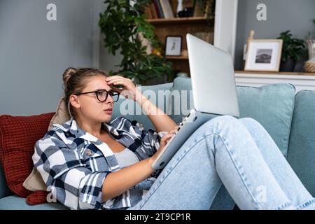 Confused young woman looking on laptop at home feeling bewildered by no connection, reading online news in internet, annoyed teen girl angry with stuc Stock Photo