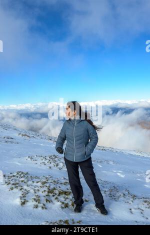 middle-aged latina woman on a snow-capped mountain above the clouds, Stock Photo