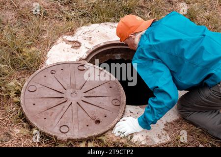 A worker leaned over the well to check the water meter. Plumbing work in rural areas. Stock Photo