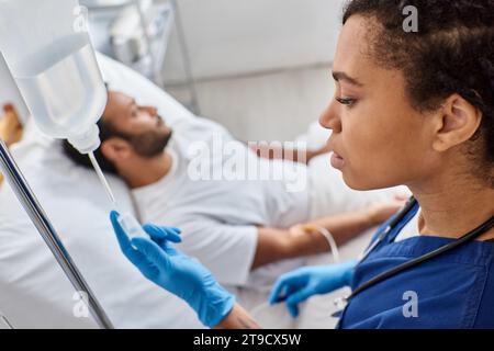 focus on african american nurse setting drop counter next to her blurred indian male patient Stock Photo