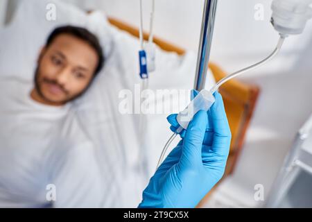 focus on african american nurse setting drop counter next to blurred man lying in hospital bed Stock Photo