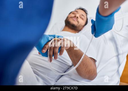 focus on african american nurse setting catheter next to blurred man lying in hospital bed Stock Photo