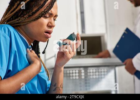 focus on african american patient using her inhaler next to her blurred indian doctor, healthcare Stock Photo