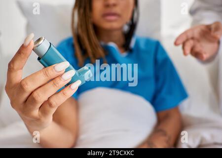 focus on asthma inhaler in hands of african american patient with doctor next to her in ward Stock Photo