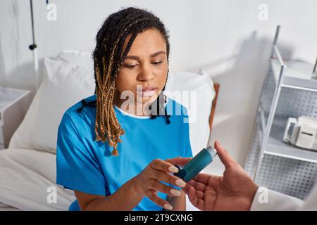 ill african american patient in hospital ward taking inhaler from her indian doctor, healthcare Stock Photo